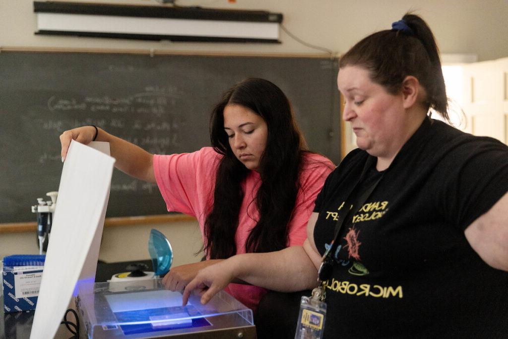 Sarah Harper Roche and Gracie Oliver put a sample into a machine in the lab. 